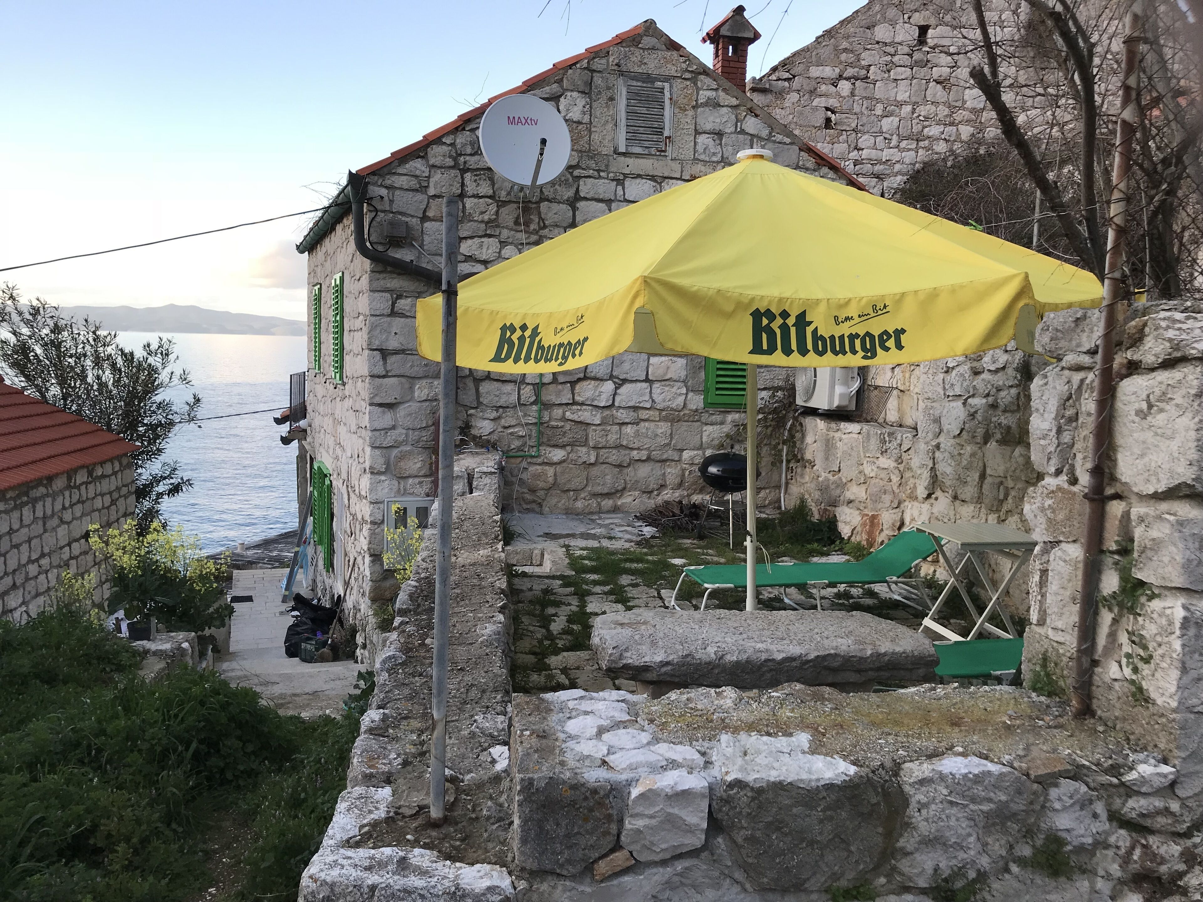 A stone building with a yellow umbrella labeled 'Bitburger' and a satellite dish.