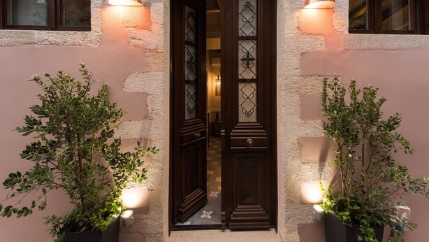 A building entrance with a wooden door, two wall-mounted lights, and potted plants on either side. - Historic restored 2-bedroom home in Old Town Chania, luxury & comfort (Chania)