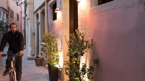 A narrow street with a person on a bicycle, potted plants, and a building with illuminated windows. - Historic restored 2-bedroom home in Old Town Chania, luxury & comfort (Chania)