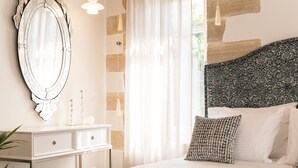 A bedroom with a bed, a dresser, a mirror, and a window with curtains. - Historic restored 2-bedroom home in Old Town Chania, luxury & comfort (Chania)