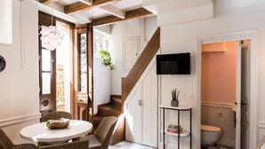 A compact living space with a dining area, a staircase, a television, and a small bathroom. - Historic restored 2-bedroom home in Old Town Chania, luxury & comfort (Chania)