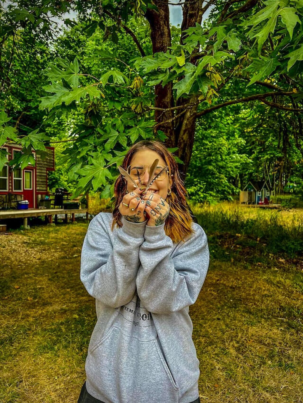 A person sitting outdoors with trees and a small building in the background.