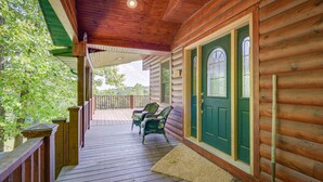 Une véranda en bois avec une porte verte, deux chaises et une petite table.