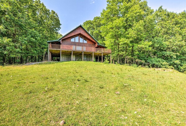 Een houten chalet met twee verdiepingen en een balkon, omringd door een dicht bos.