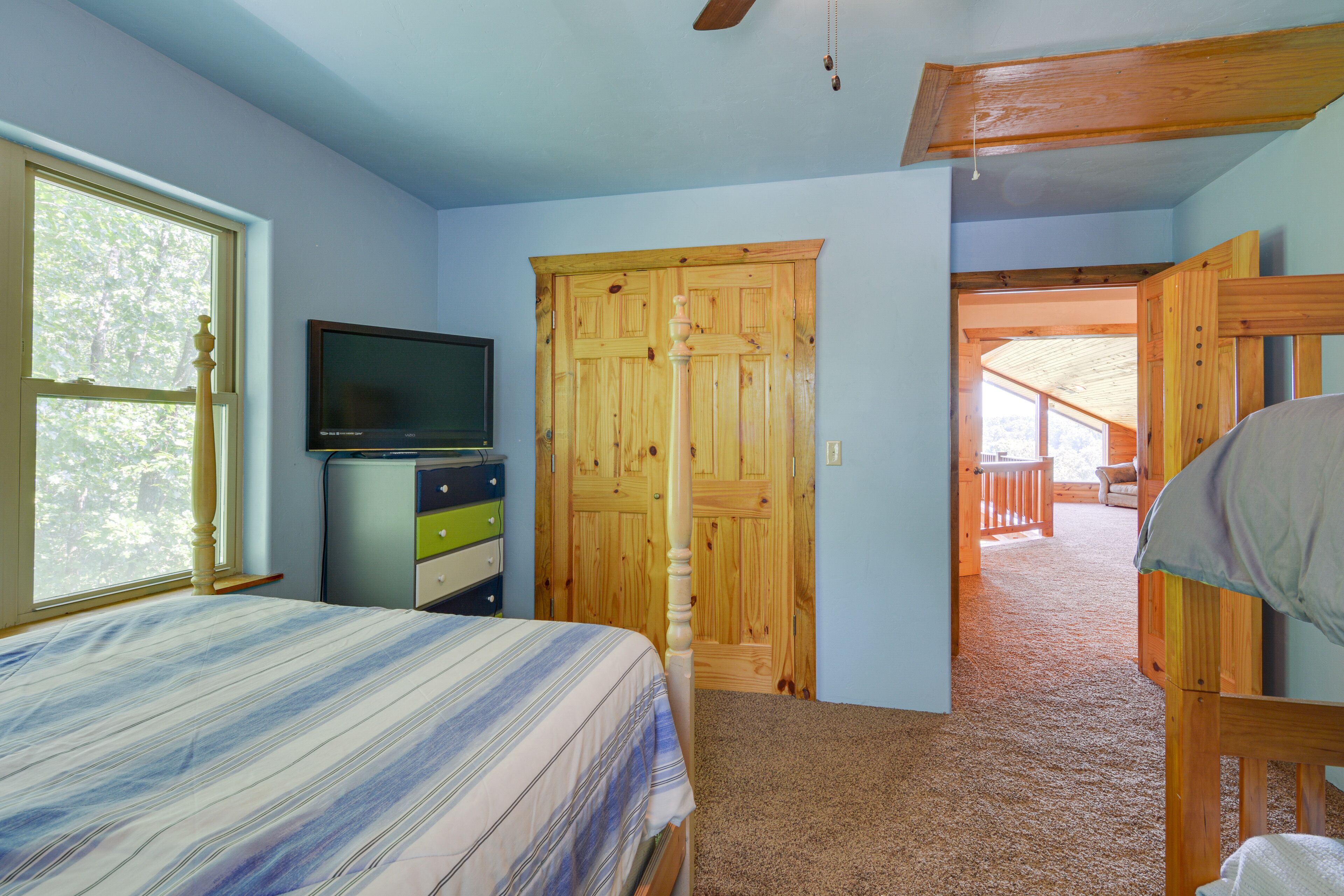 A bedroom with a bed, a television, a dresser, and a wooden door leading to a balcony.