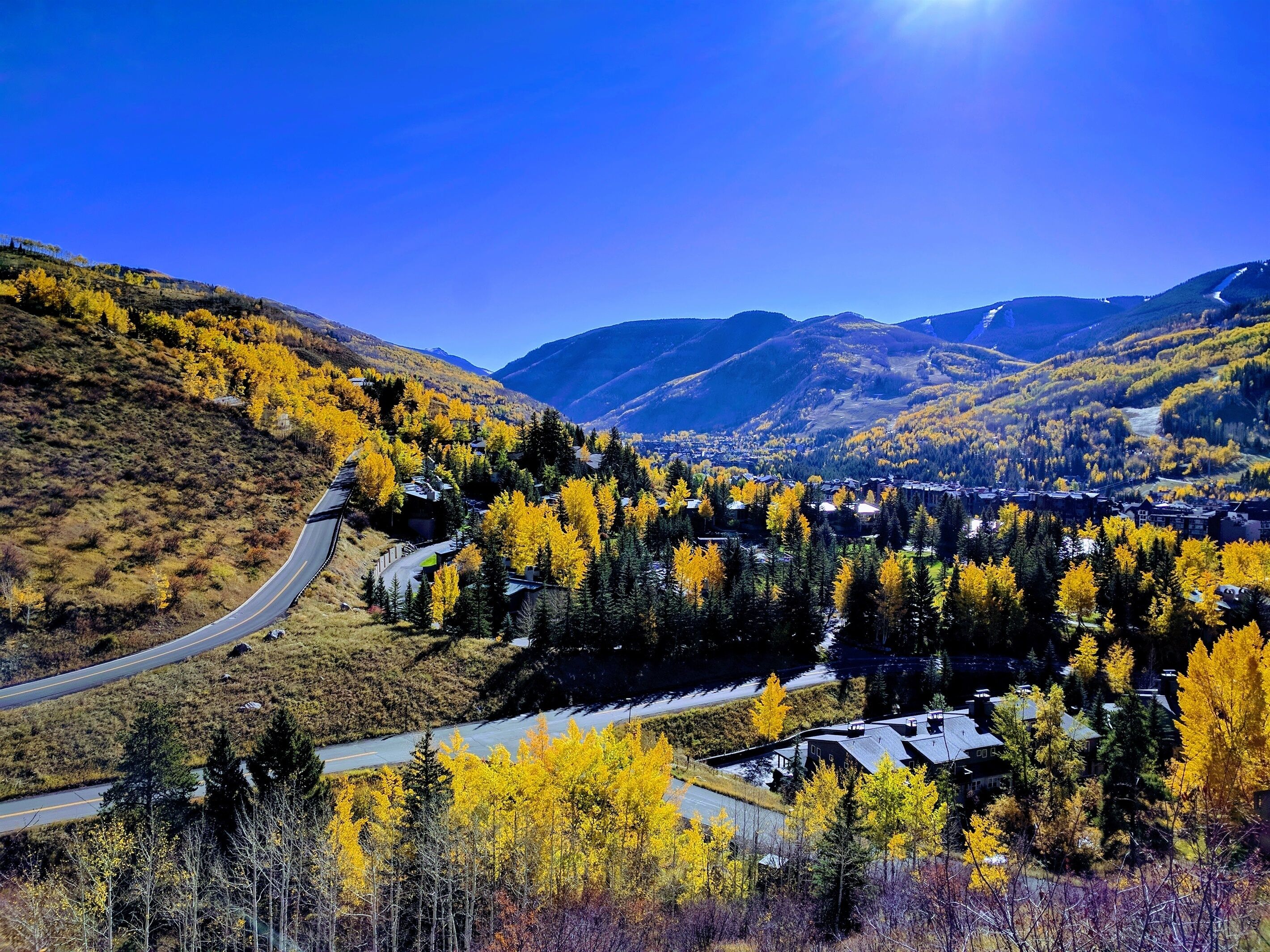 A winding road through a valley with autumn-colored trees and a mountain backdrop.