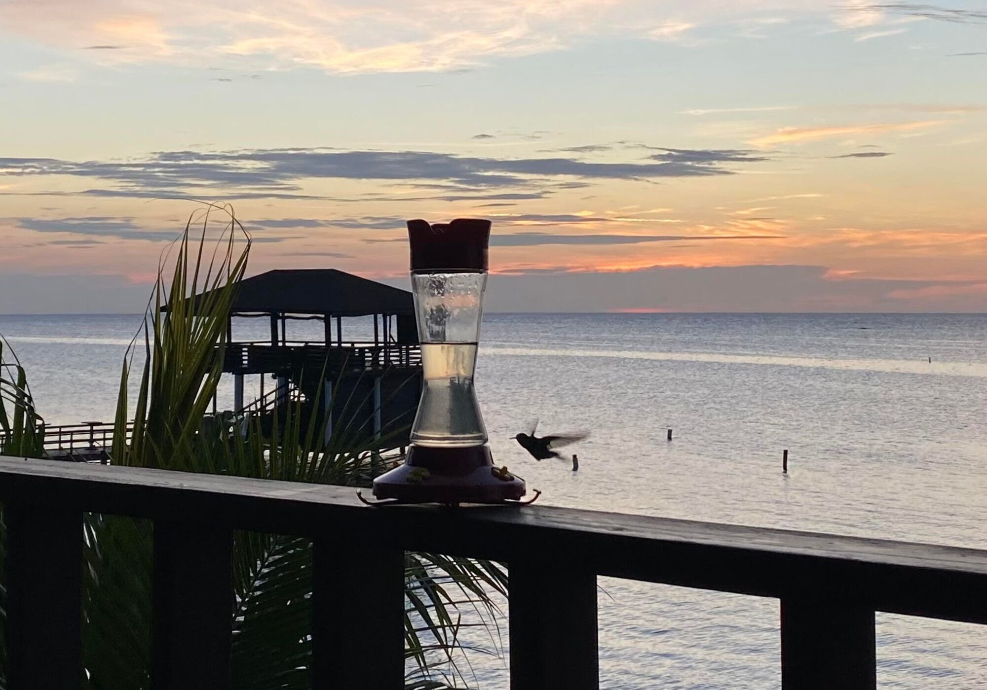 A glass sculpture on a balcony overlooking a body of water with a sunset in the background.
