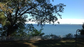 A view of a body of water with a distant structure, a white picket fence, and a tree in the foreground. - Oceanfront Beach House In Plymouth (Plymouth)