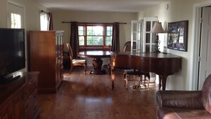 A spacious living room with a wooden floor, a television, a piano, and a dining table. - Oceanfront Beach House In Plymouth (Plymouth)