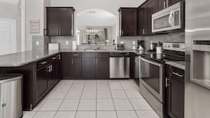 A modern kitchen with dark cabinetry, stainless steel appliances, and a tiled floor.
