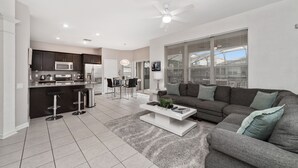 A modern living room with a gray sofa, a white coffee table, and a kitchen area with dark cabinets and a white refrigerator.