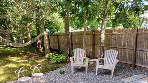 Ein Garten mit zwei Adirondack-Stühlen, einer Hängematte und einem Holzzaun.