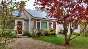 Ein eingeschossiges Haus mit geneigtem Dach, Solaranlagen, einer roten Tür und einem gepflegten Vorgarten mit Baum und Sträuchern.