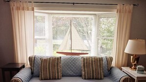 Ein Zimmer mit einer Couch, einer Lampe und Blick auf ein Segelboot durch ein Fenster mit Jalousien.