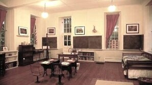 Un aula con mobiliario de madera, una pizarra y cuadros en las paredes.