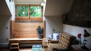Una habitación acogedora con un banco de madera, un sofá de cuadros, una mesita y una ventana con vistas a la vegetación.
