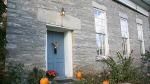 Un edificio de piedra con una puerta azul, dos calabazas y un arreglo floral.