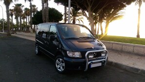 A black van parked on a street with palm trees and a grassy area in the background. - Adeje Tijoco Alto Overseas Real Estate Villa (Palm-Mar)