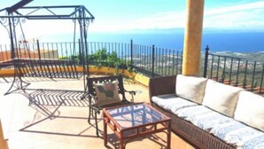 A balcony with a sofa, a table, and a swing set. - Adeje Tijoco Alto Overseas Real Estate Villa (Palm-Mar)