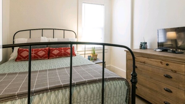 A bed with a metal frame, a wooden dresser, and a television on top. - Mid-Century Modern Home in Downtown Royal Oak! (Royal Oak)