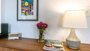 Een houten nachtkastje met een lamp, een vaas met bloemen, een fotolijstje en een tijdschrift.