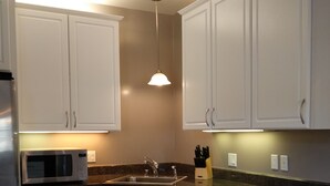 Una cocina moderna con armarios blancos, un refrigerador de acero inoxidable, microondas, pileta y lavavajillas.
