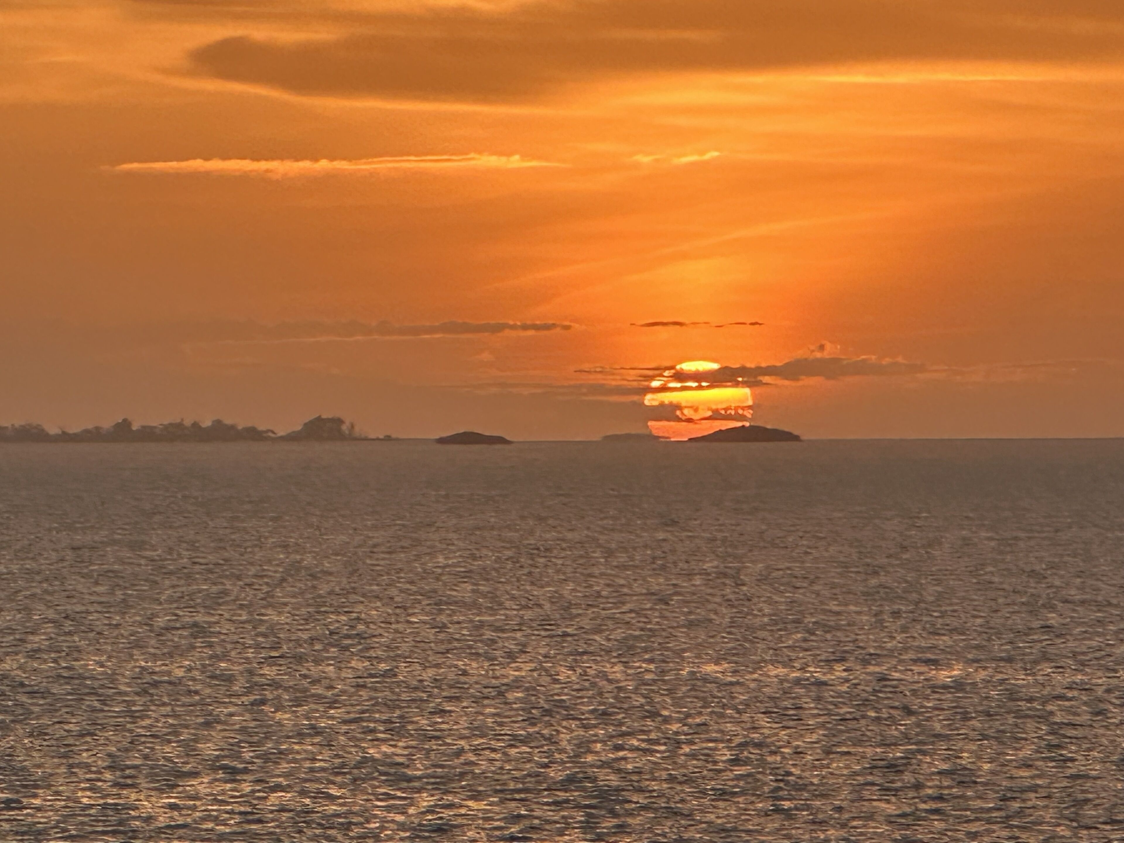 Um pôr do sol sobre um mar tranquilo com silhuetas distantes da terra.