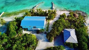 An aerial view of a coastal property with a blue-roofed building, a white-roofed structure, and a sandy beach. - Bonefish Bella Vista - Beachfront Retreat, Tropical Garden & Natural Ocean Pool (Georgetown)