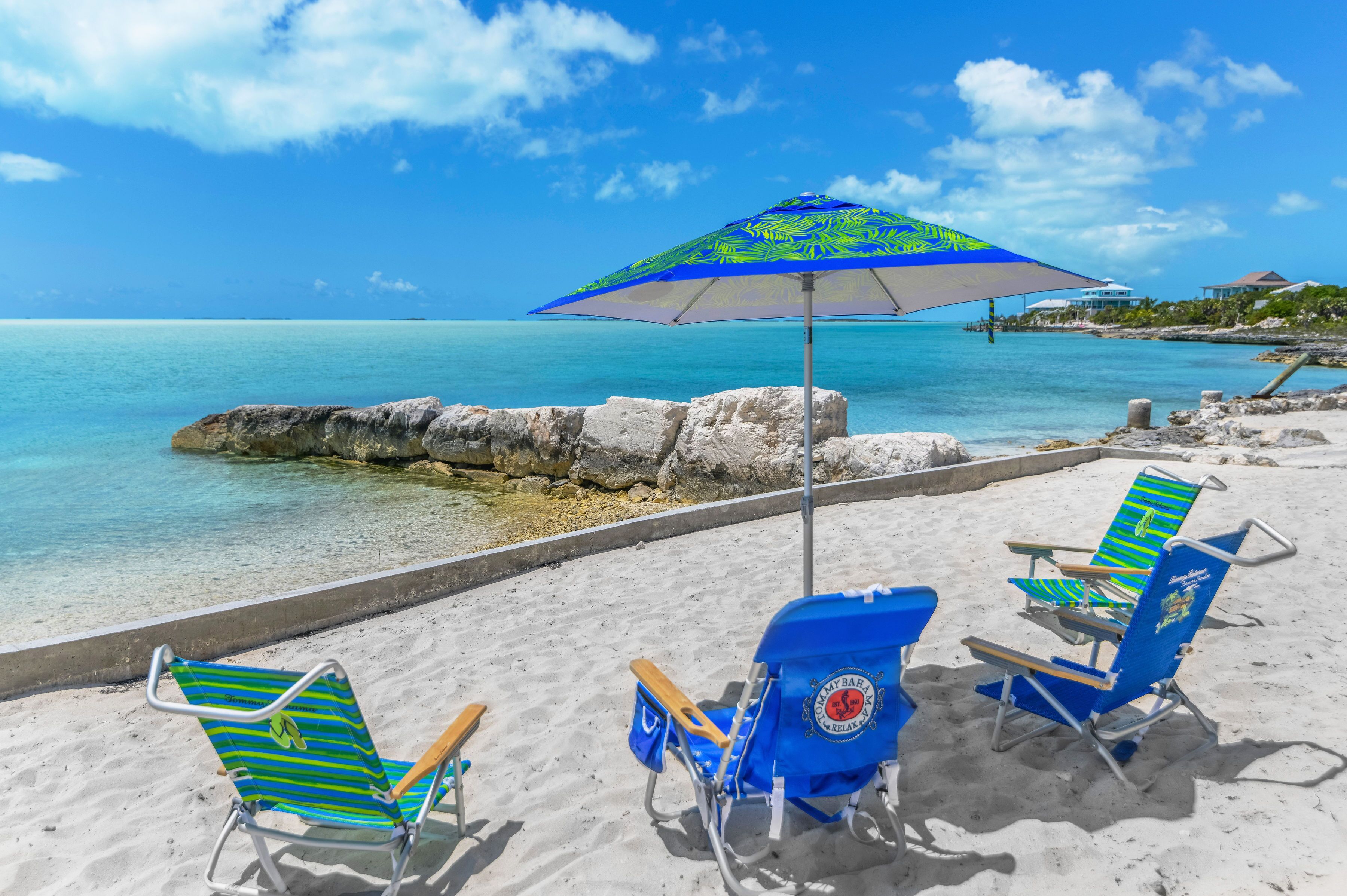 Una spiaggia con due sdraio blu e un ombrellone grande, un cielo azzurro terso e acqua turchese calma.
