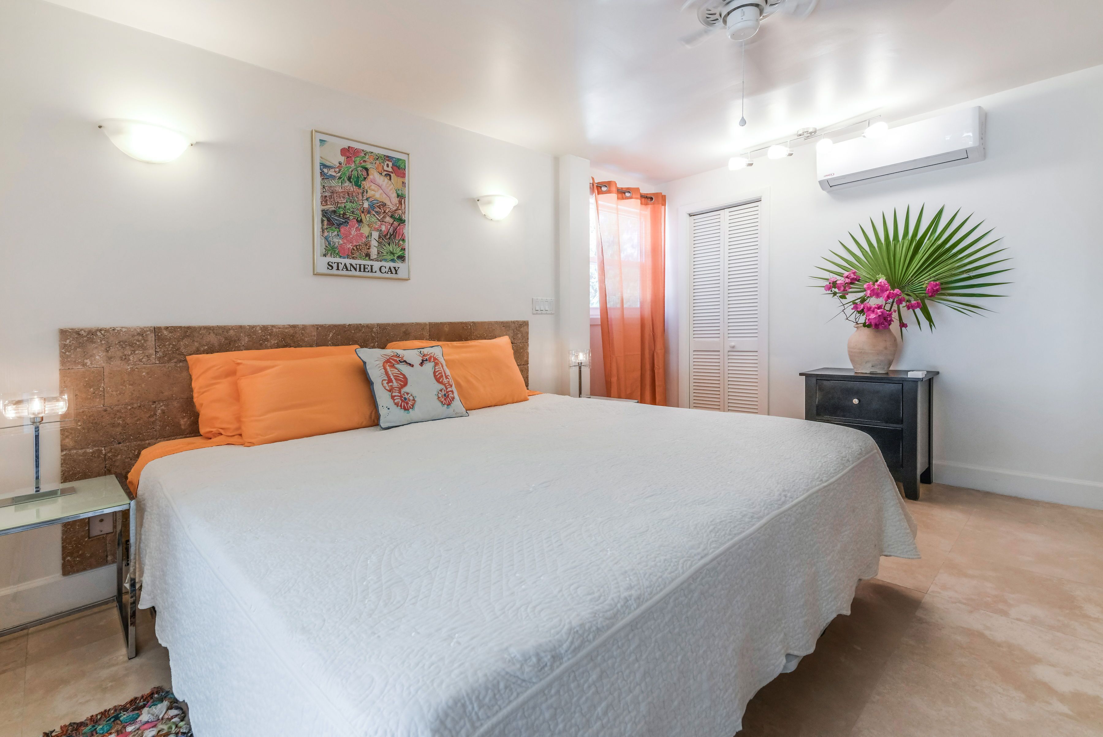 Une chambre à coucher bien aménagée, avec un grand lit, une table de chevet, une commode, un climatiseur fixé au mur et un élément décoratif mural.