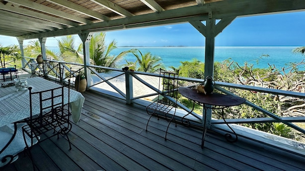 A wooden deck with a table and chairs, overlooking a beach and ocean. - Bonefish Bella Vista - Beachfront Retreat, Tropical Garden & Natural Ocean Pool (Georgetown)