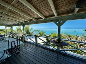 A wooden deck with a table and chairs, overlooking a beach and ocean.