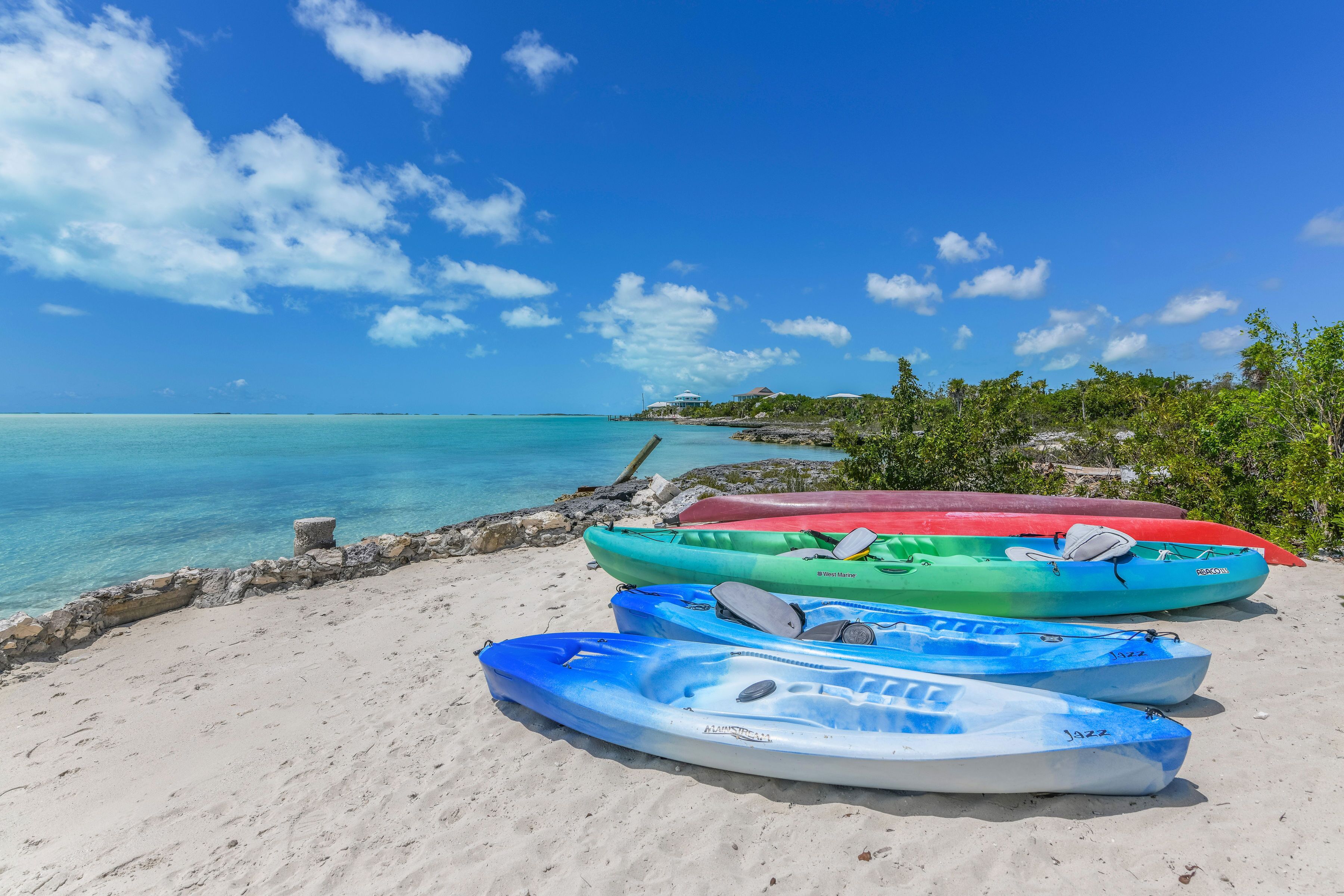 Una playa con kayaks alineados en la arena, un cielo azul despejado y agua turquesa tranquila.