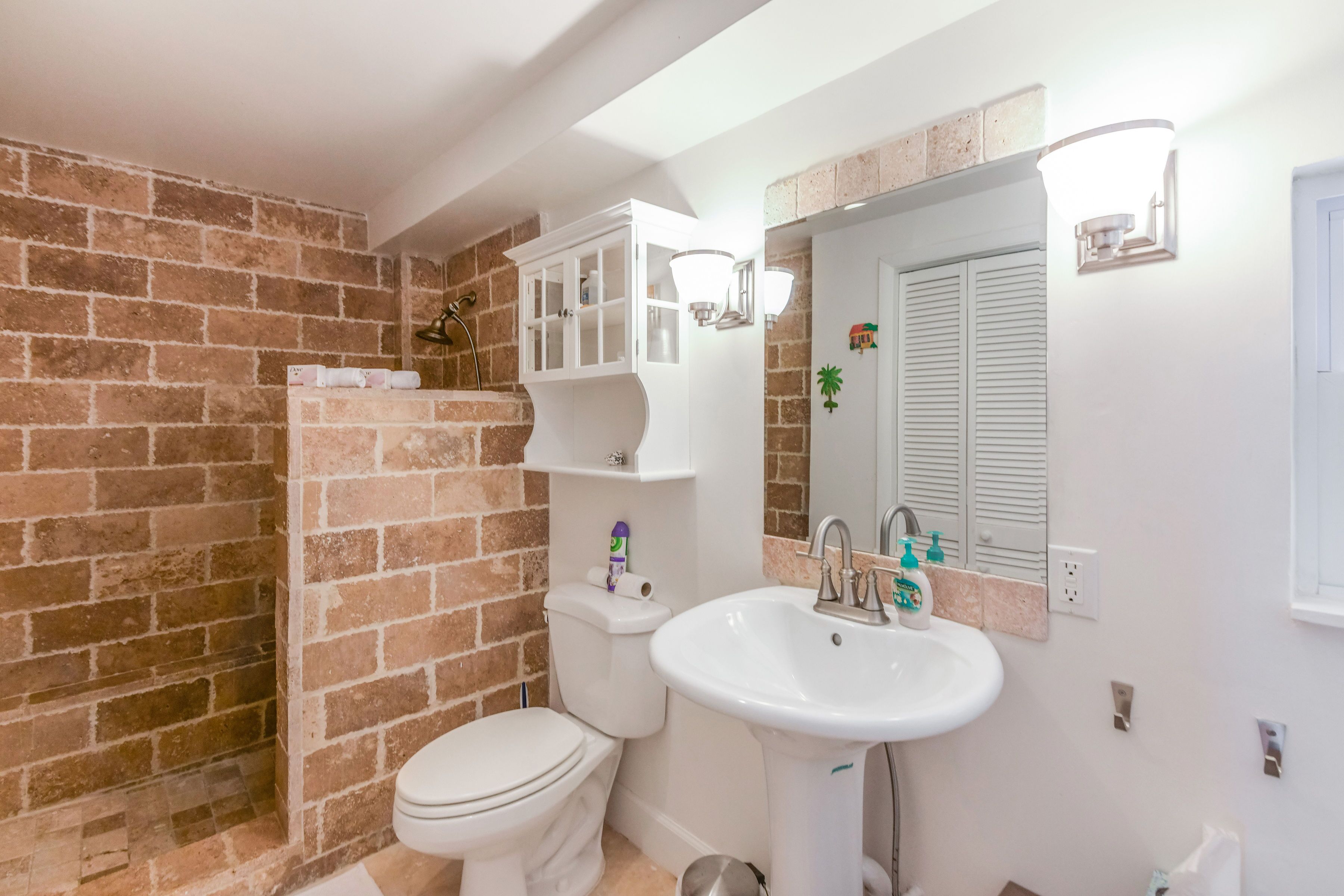 Un baño con pared de ladrillo, un inodoro, un lavabo y un armario con estantes.