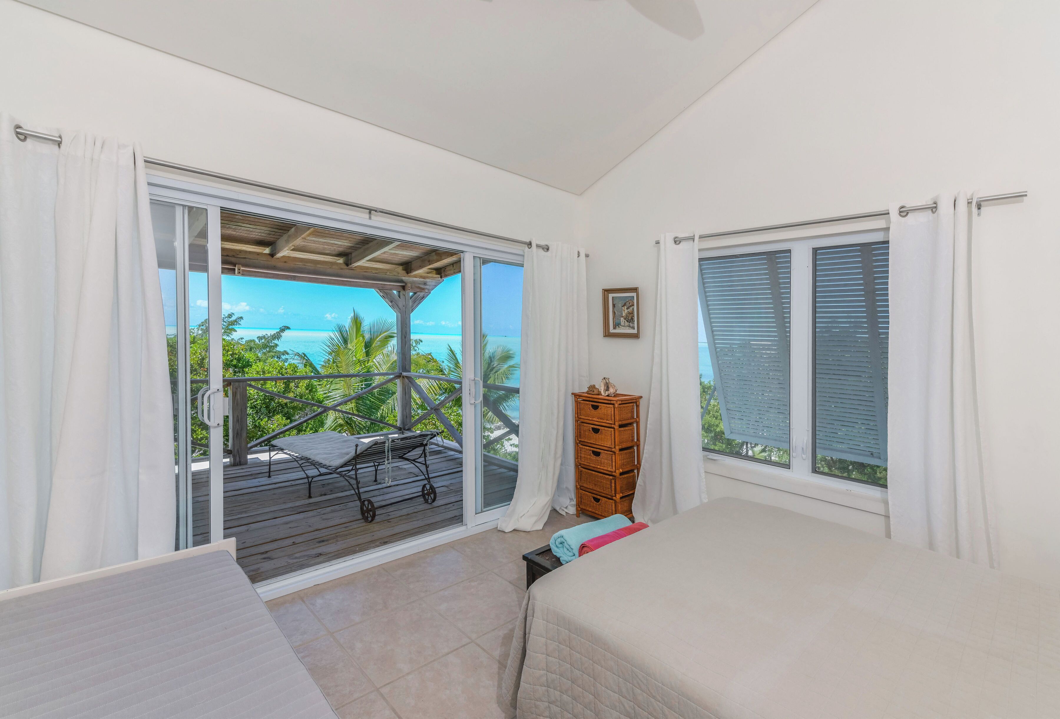 A bedroom with a large sliding glass door leading to a balcony with a view of the ocean.
