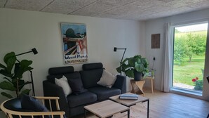 A modern living room with a sofa, a chair, a coffee table, and a large window. - Agermosegaard Hyggeligt Feriehus – Landlig idyl i Barløse, Fyn Golf & Cykelruter (Assens)