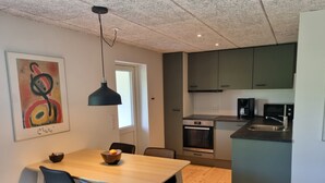 A modern kitchen with a built-in oven, microwave, and sink. There is a dining area with a wooden table and black chairs. - Agermosegaard Hyggeligt Feriehus – Landlig idyl i Barløse, Fyn Golf & Cykelruter (Assens)