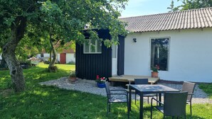 A small, modern house with a tiled roof, a wooden deck, and a table with chairs. - Agermosegaard Hyggeligt Feriehus – Landlig idyl i Barløse, Fyn Golf & Cykelruter (Assens)