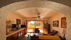Una sala de estar acogedora con un sofá, una mesa de centro y un televisor. Se observa un dispensador de agua grande y un ventilador de techo.