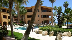 Un resort con piscina, palmeras y un edificio con varios balcones.