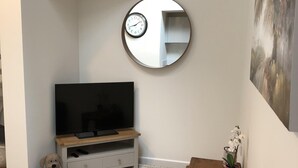 A bedroom with a bed, a TV on a wooden stand, a round mirror, a small table with a plant, and a dog. - Perfect for walkers, Goodwood, National Trust, Short Stay (Bramshott Chase)