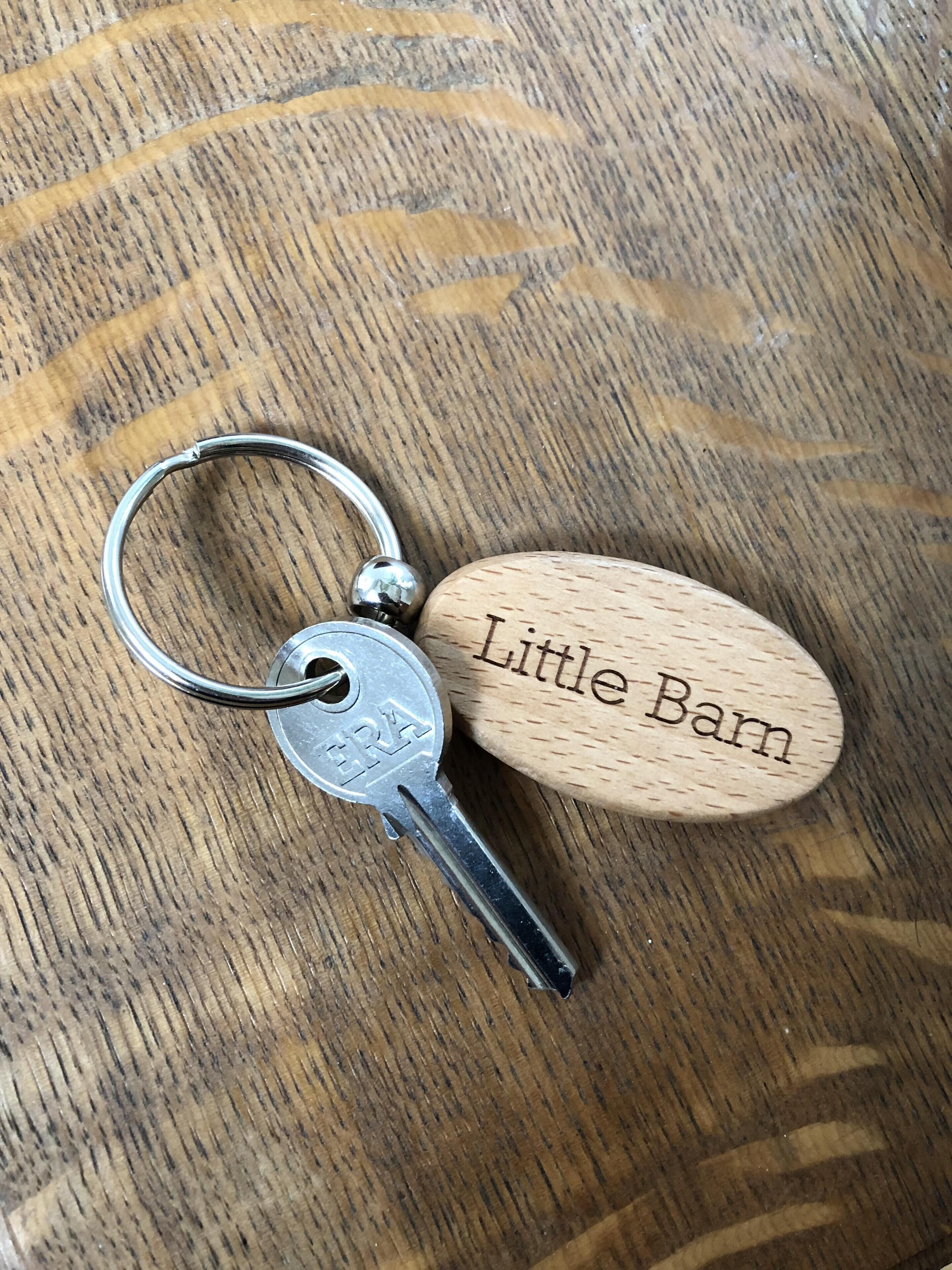 Un llavero con una llave metálica y una etiqueta de madera que dice 'Little Barn'.