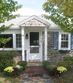 Traditional home with a central entrance, flanked by windows, surrounded by lush greenery.