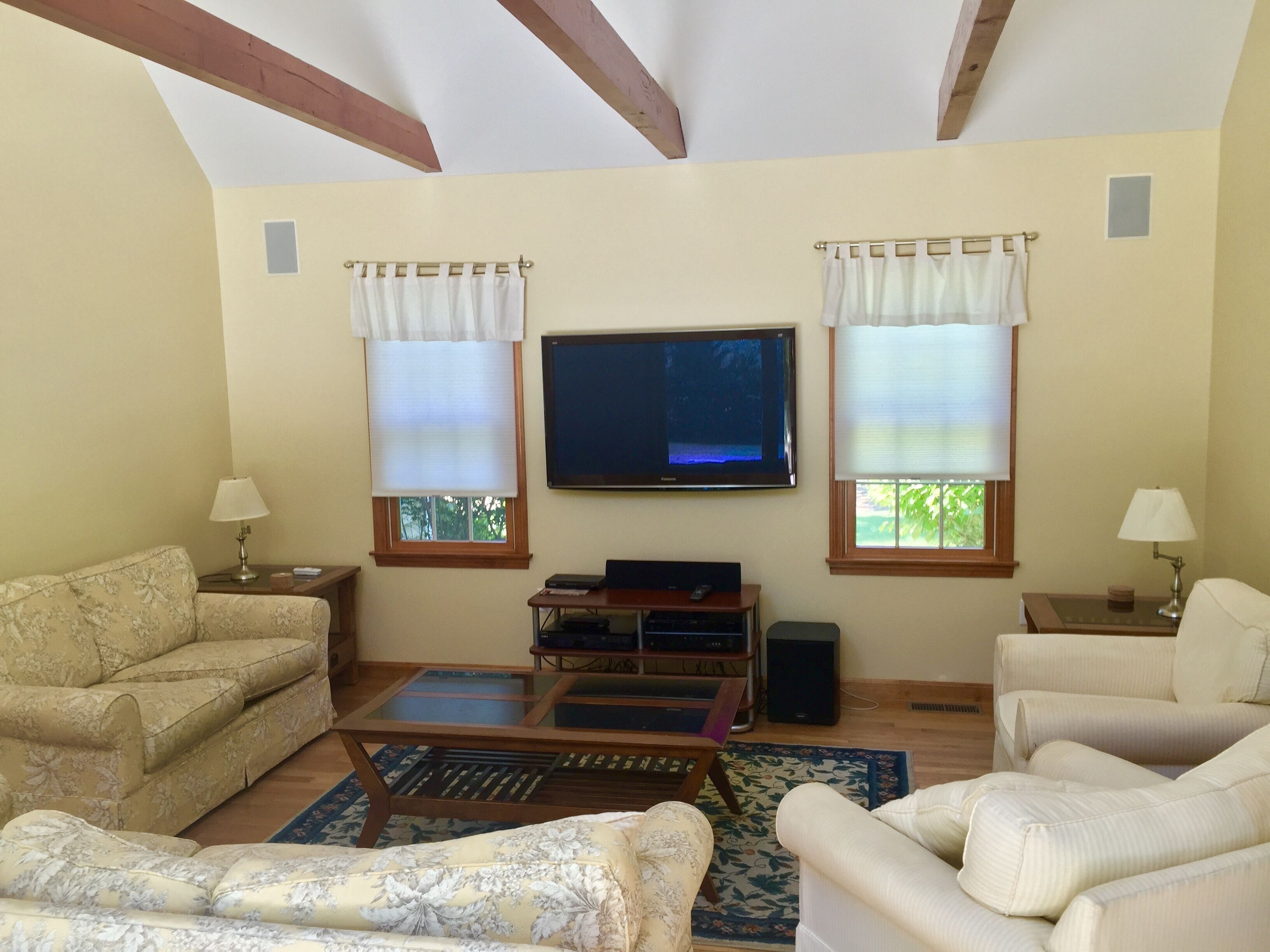 A living room with two sofas, a coffee table, a flat-screen TV, and two windows with curtains.