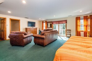 A bedroom with a large bed, two leather sofas, a wooden dresser, a television, and a sliding glass door leading to a balcony.