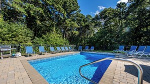 A rectangular swimming pool with a metal safety railing, surrounded by blue lounge chairs and a grill.