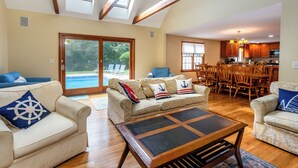 A spacious living area with a large window, a pool, and a dining area with wooden furniture.