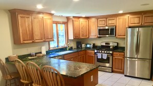 A kitchen with wooden cabinets, a stainless steel refrigerator, a microwave, and a stove. There are four wooden chairs around the island.