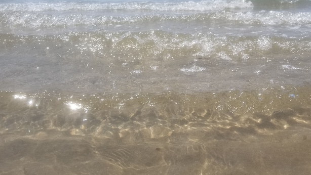 Een strand met helder water en golven.