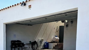 Een garage met een tafel, stoelen, een blauwe watertank en een wit voertuig.